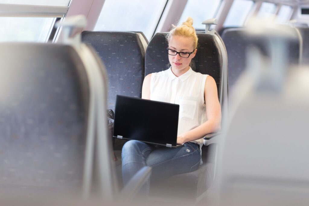 Henkilö istuu lentokoneessa kannettava tietokone sylissä.